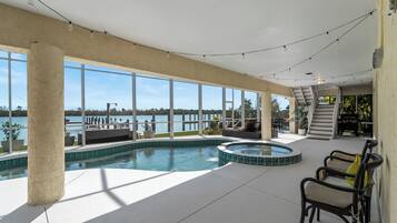 Un vaste espace intérieur abritant une piscine, avec vue sur le plan d’eau extérieur, un jacuzzi et un escalier menant à un niveau supérieur.