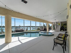 A spacious indoor pool area with a view of the water body outside, a hot tub, and a staircase leading to an upper level.