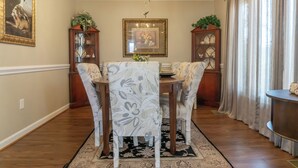 Une salle à manger agrémentée d’un lustre, de deux buffets en bois aux portes vitrées, d’une table à manger et de quatre chaises recouvertes d’un tissu à motifs floraux.