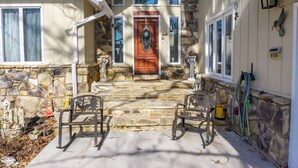 Une maison avec une façade en pierre, une porte d’entrée en bois ornée d’une guirlande, et deux fauteuils à bascule placés à l’extérieur.