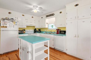 A kitchen with white cabinets, a teal countertop, a ceiling fan, and a sign labeled 'SEASIDE.' - 321 Packed with Amenities and Close to the Beach! (Kill Devil Hills)