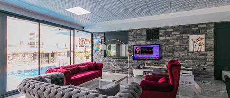 A modern living room with a stone wall, a large TV, and a pool view.