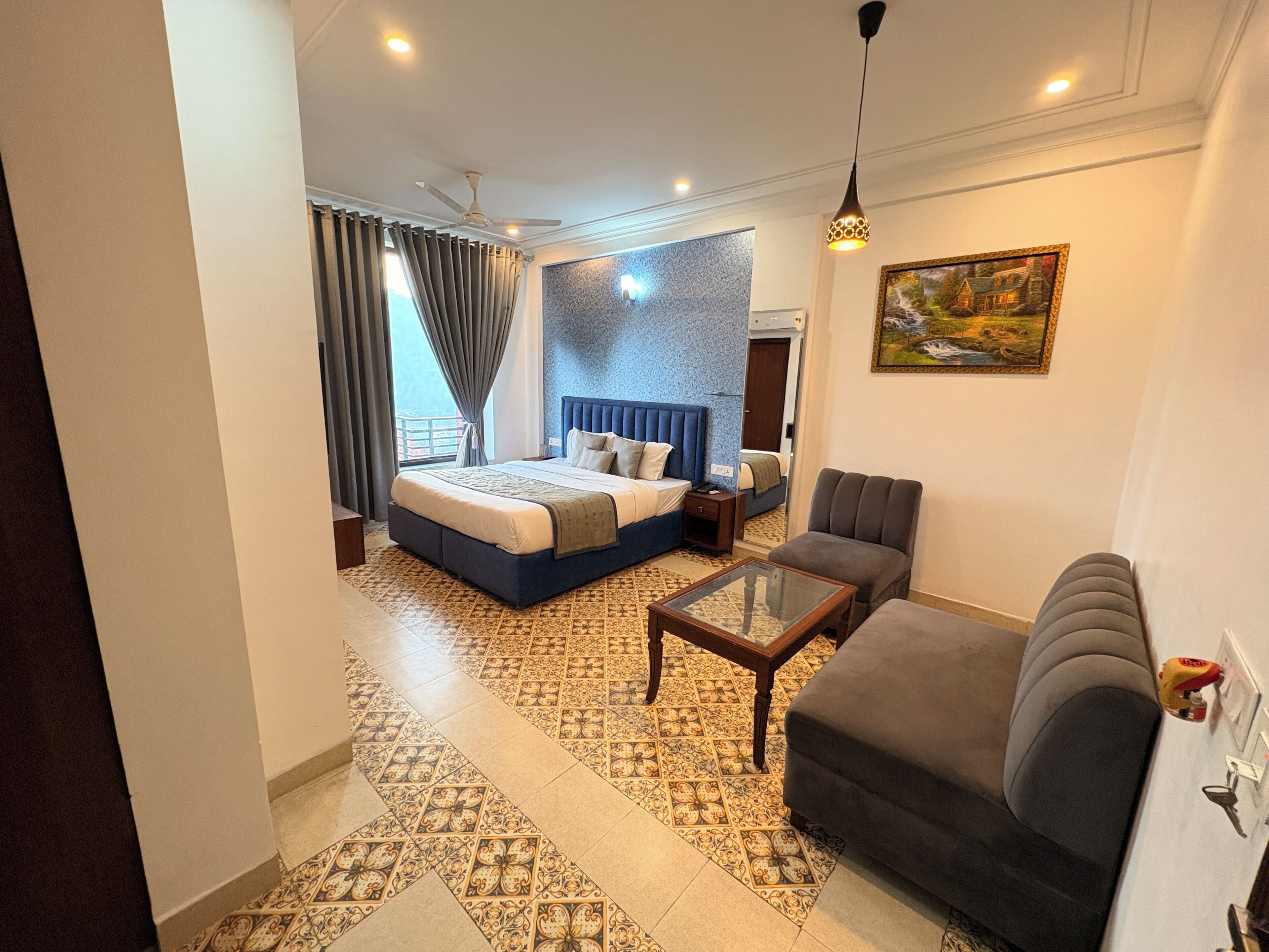 Une chambre d’hôtel comprenant un lit, un canapé, une table basse, un tableau et un revêtement de sol à motifs.