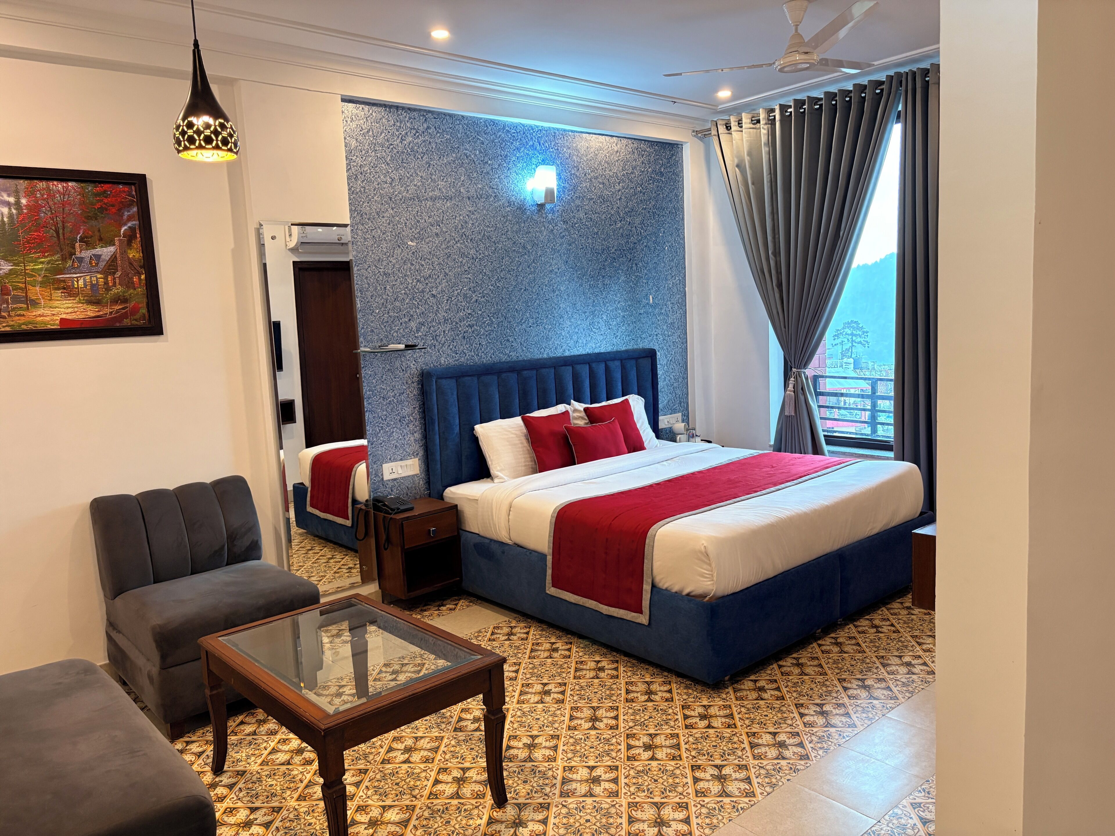 Habitación de hotel con una cama grande, un sofá, una mesita, un cuadro y un suelo estampado.