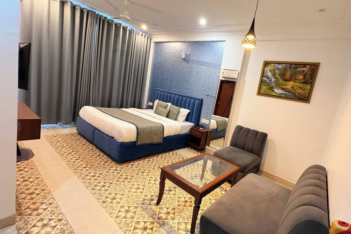 Habitación de hotel con una cama, un sofá, una mesa de centro, un televisor y un cuadro en la pared.