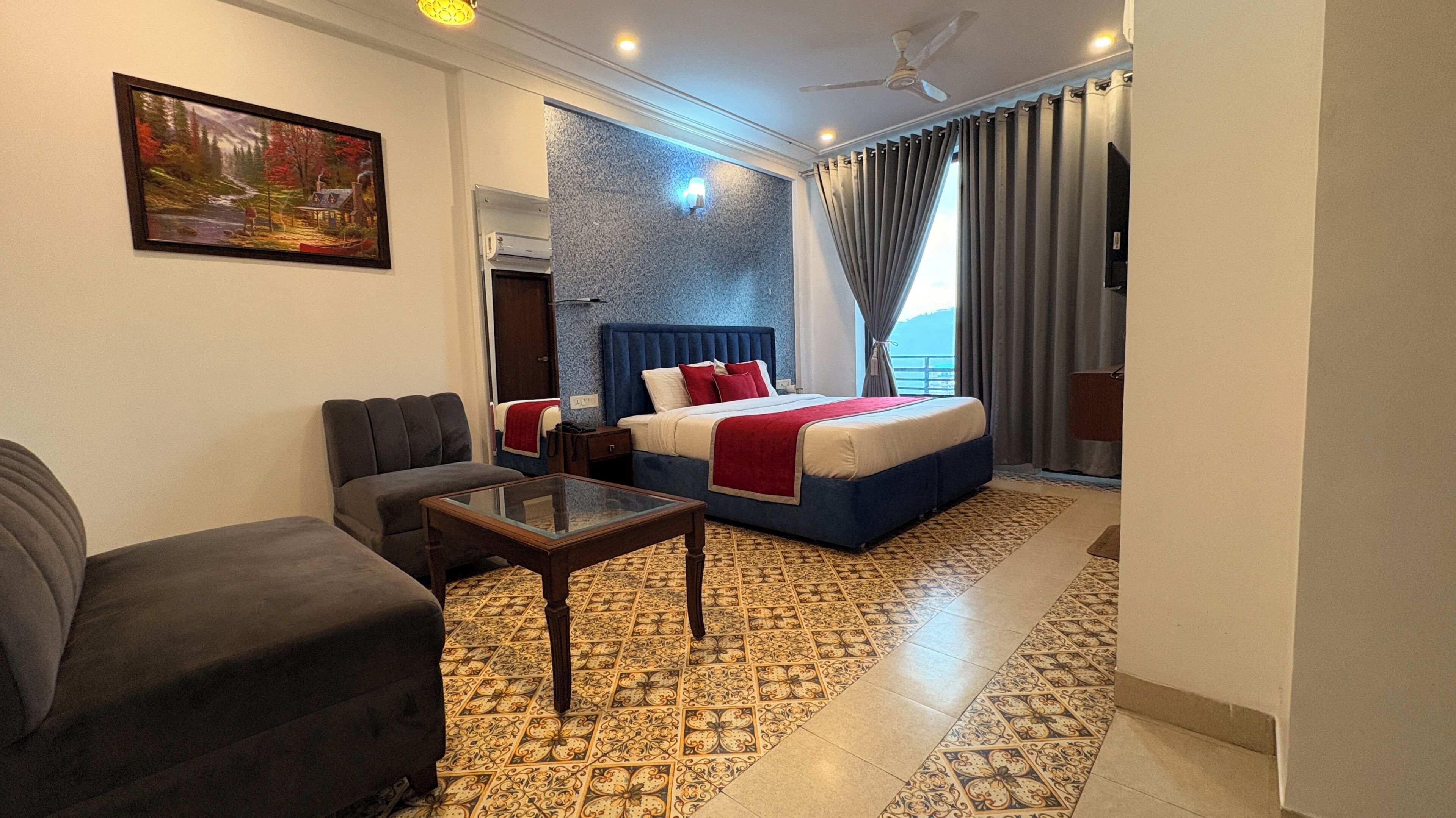 A hotel room with a bed, a sofa, a small table, a painting on the wall, and a view of the sea.