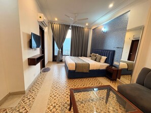Une chambre d’hôtel avec un lit, une télévision, un ventilateur de plafond, une fenêtre avec des rideaux et un sol à motifs.