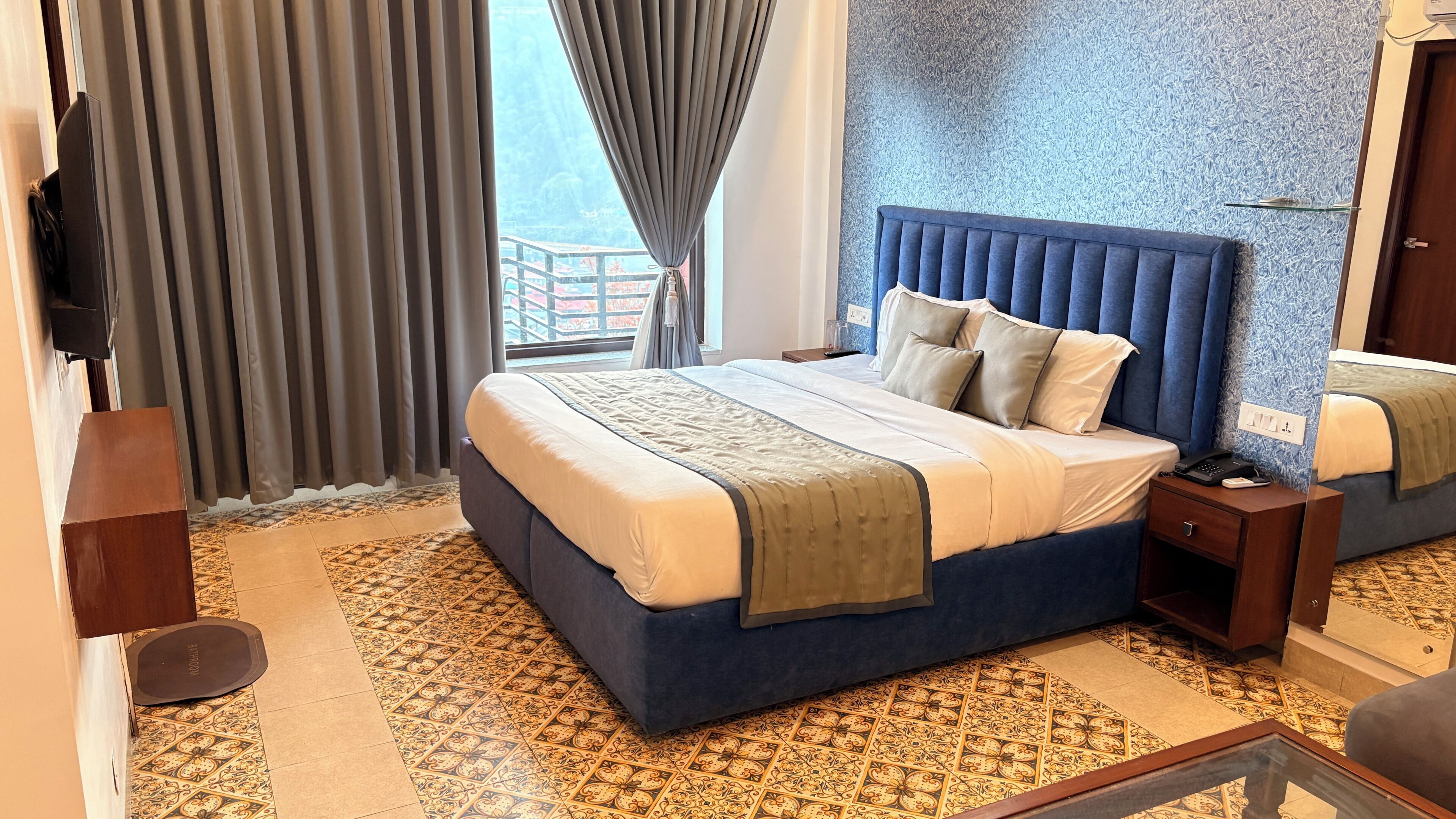 A hotel room with a large bed, a nightstand, a TV, and a view of the outside.