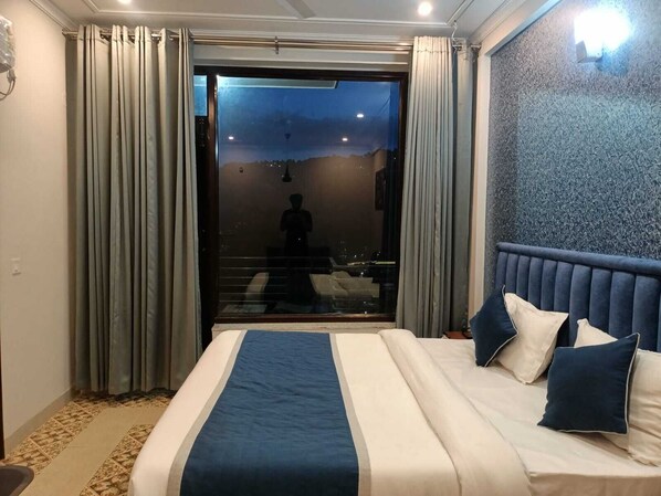 A hotel room with a large bed, a view through the window, and a patterned wall. - Barog Residency (Solan)