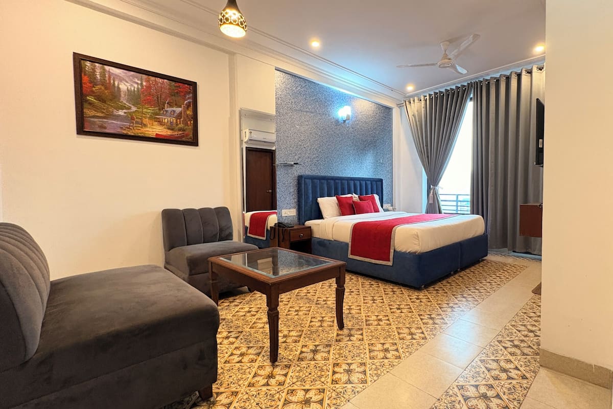 Habitación de hotel con cama, sofá, mesa de centro de vidrio, un cuadro en la pared y piso con diseño.