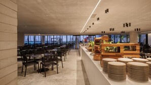 A spacious indoor area with multiple tables and chairs, a long counter with stacked plates, and a view through large windows. - Porto alto resort  (Ipojuca)