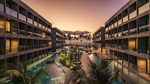 A hotel with a central pool surrounded by palm trees and outdoor seating, featuring multiple floors with balconies. - Porto alto resort  (Ipojuca)
