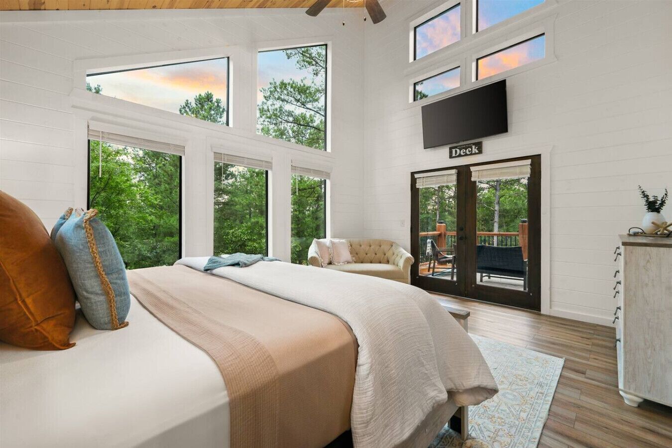 A bedroom with a large bed, a sofa, a TV, and a deck area.