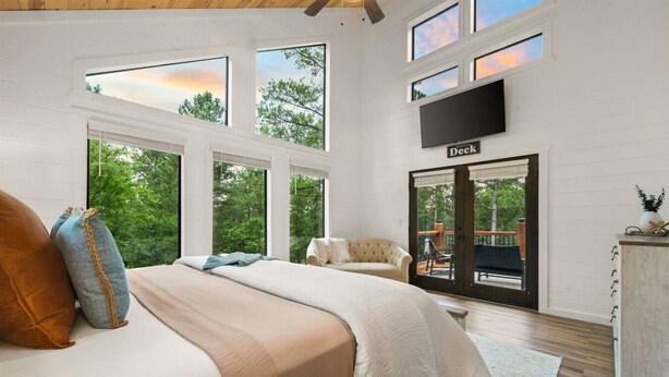 A bedroom with a large bed, a sofa, a TV, and a deck area. - The Grinning Bear|Sleeps 14|Basketball|Pickleball (Broken Bow)