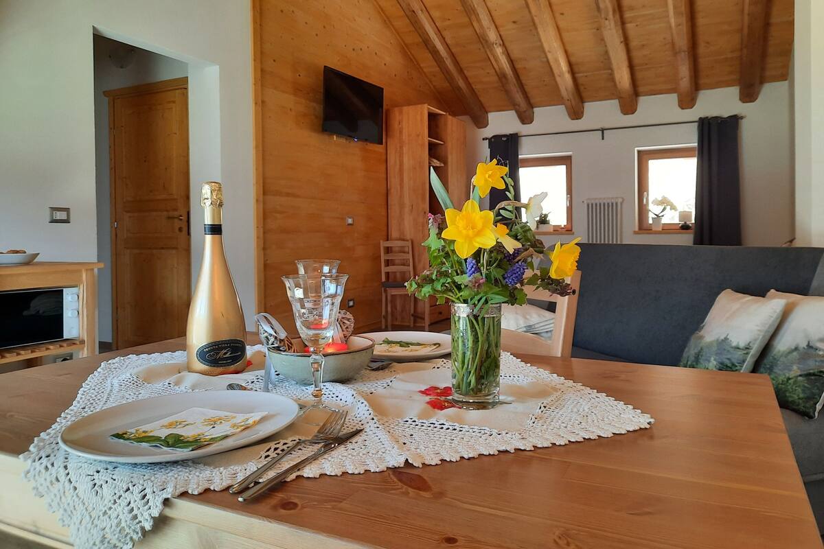 A dining table with a white lace tablecloth, a vase with yellow flowers, and a bottle of champagne.