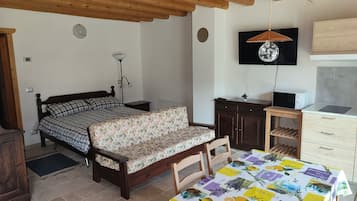 Ein Schlafzimmer mit Bett, Schreibtisch, Stuhl, Tisch, Fernseher und einer Küchenzeile.