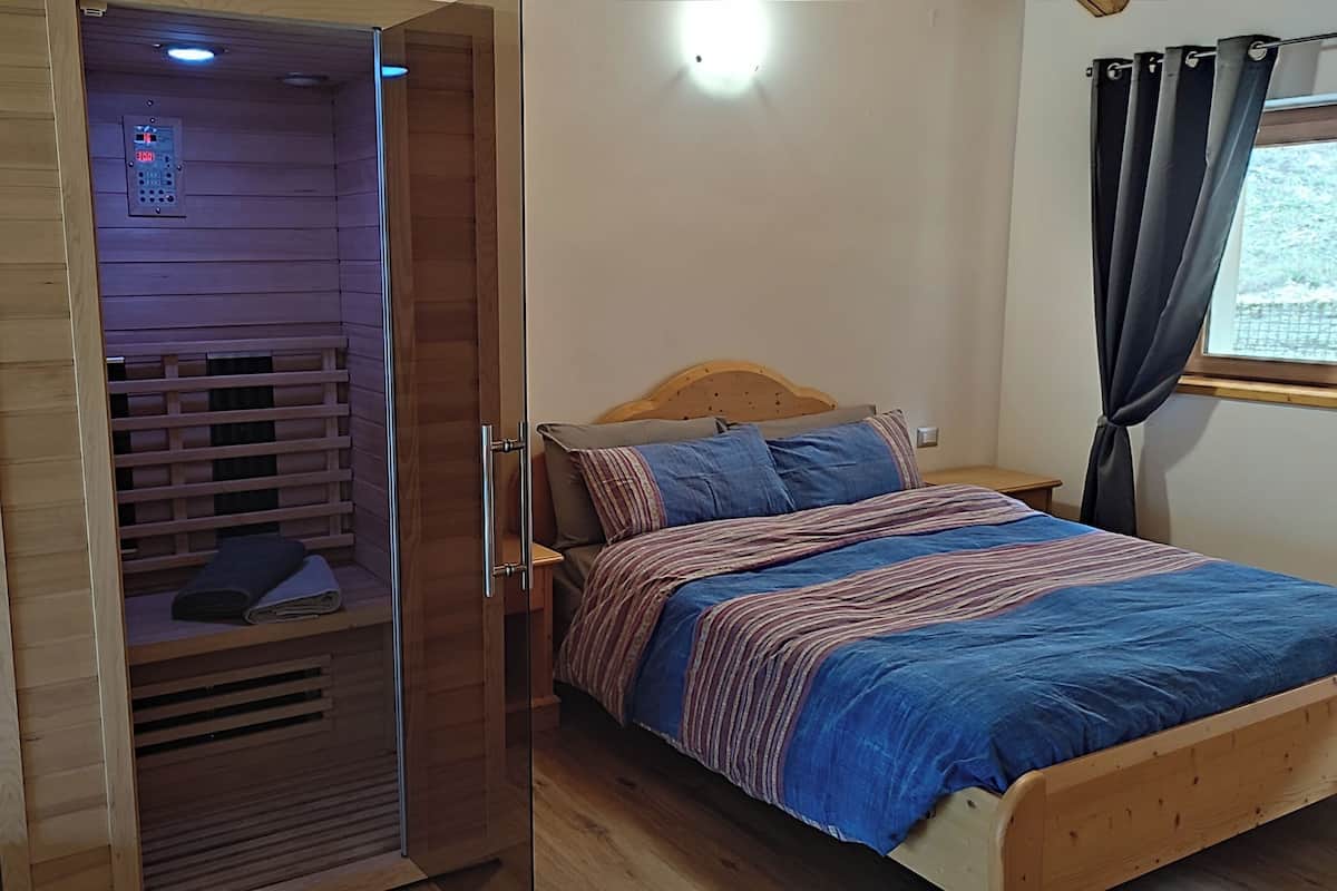A bedroom with a wooden bed, a nightstand, a wooden wardrobe with a built-in heater, and a window with curtains.