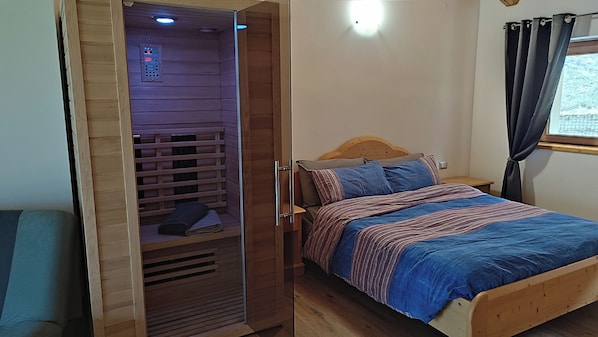 A bedroom with a wooden bed, a nightstand, a wooden wardrobe with a built-in heater, and a window with curtains. - Ai Monti (Barcis)