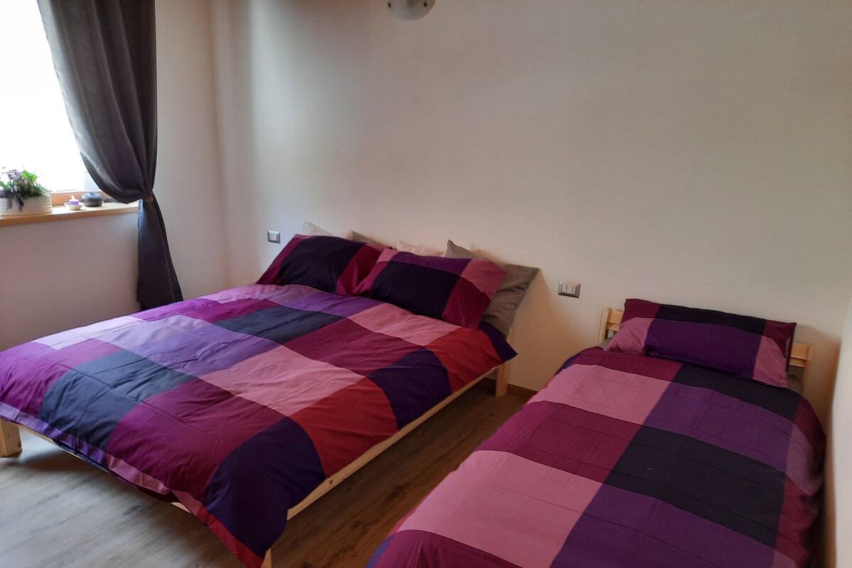 A room with two wooden beds, each with a purple and pink quilt.