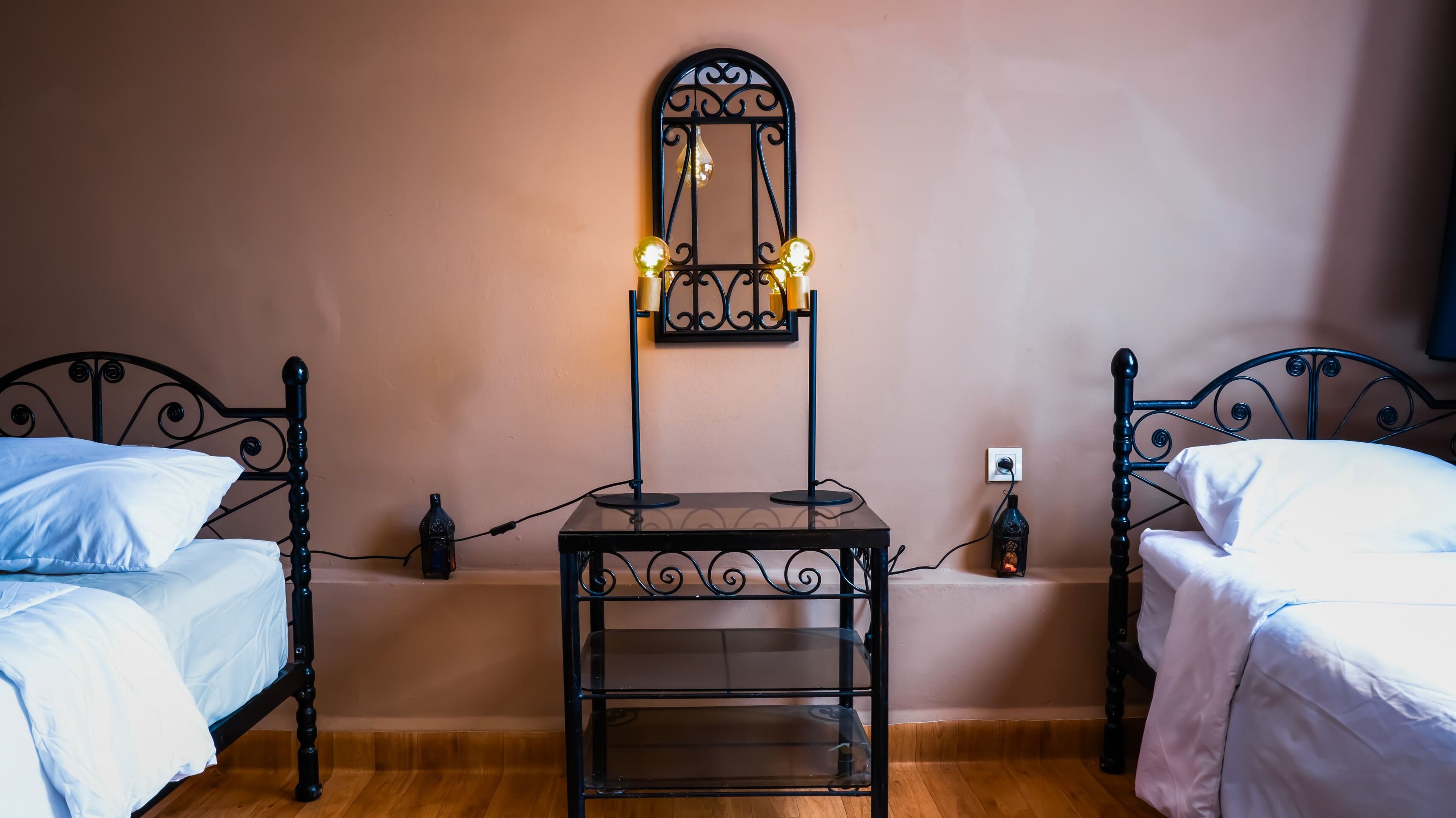 Een slaapkamer met twee eenpersoonsbedden, een klein tafeltje met spiegel en een wandlamp.