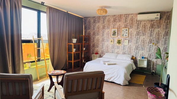 Une chambre d’hôtel avec un lit, une chaise en bois, une petite table, une bibliothèque et une fenêtre avec des rideaux.