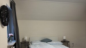 Un dormitorio con cama, lámparas de noche, un radiador, una ventana con cortinas y un adorno de pájaro anidado en la pared.