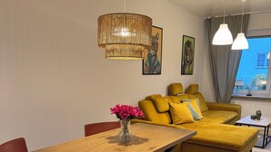 Una sala de estar moderna con una mesa de comedor de madera, sillas rojas, un banco de cuero marrón, un sofá amarillo con cojines a juego y una lámpara colgante grande de fibras.