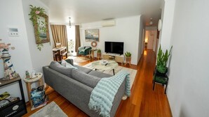 A modern living room with a grey sofa, a coffee table, and a TV. There is a plant on the side and a bookshelf with books. - 5 minutes to the beach!  (Brighton-Le-Sands)