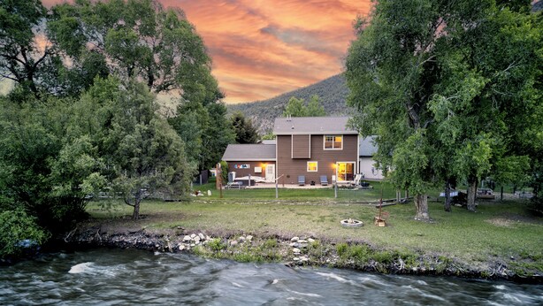 Una casa con un río al frente, rodeada de árboles y un paisaje montañoso.
