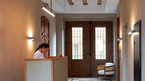 A hotel lobby with a reception desk, patterned carpet, wooden doors, and a bench. - Tradere Hotel Boutique (Moncada)
