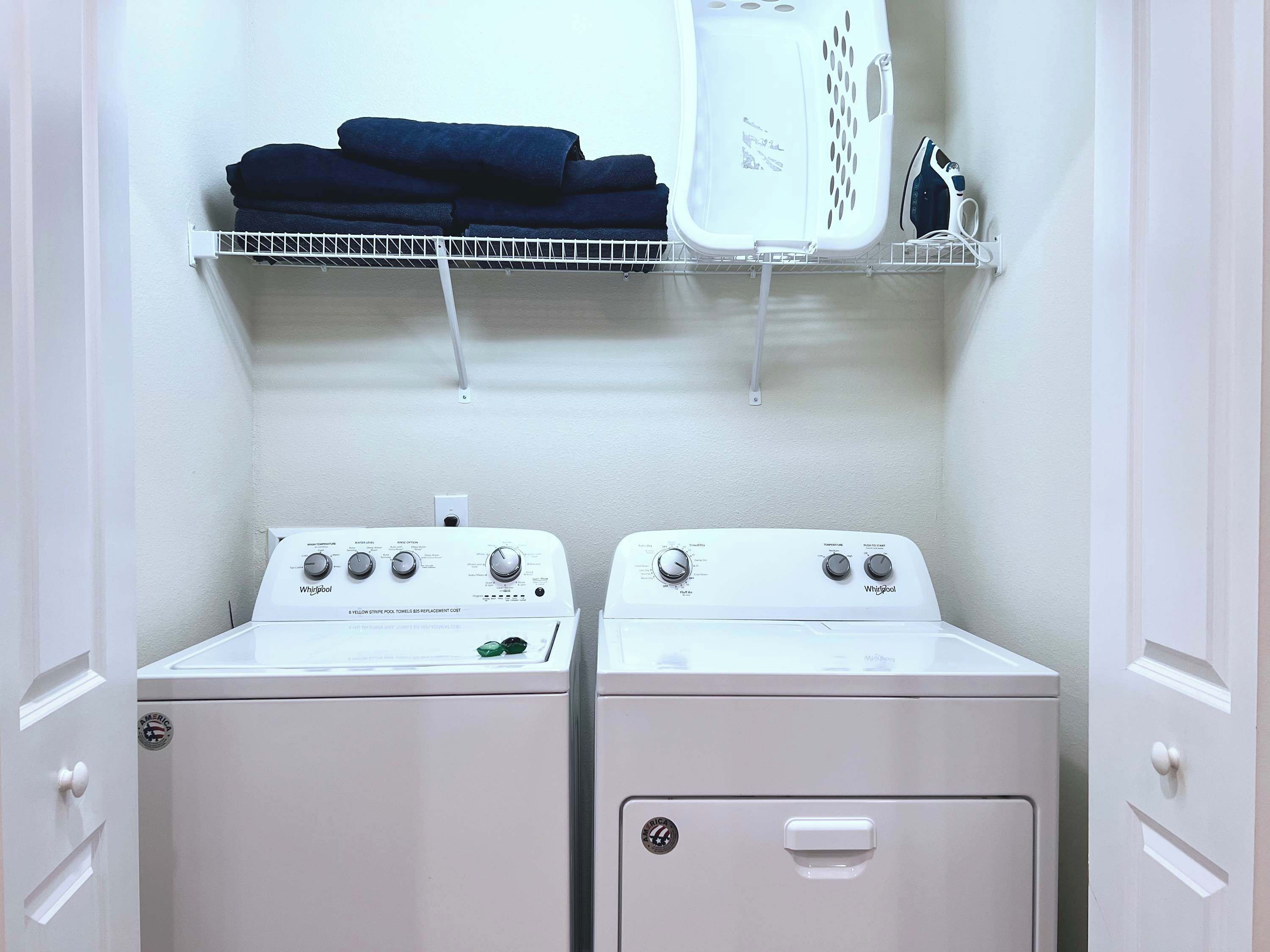 A laundry room with two stacked washers and dryers, a shelf with folded towels, and a laundry basket.