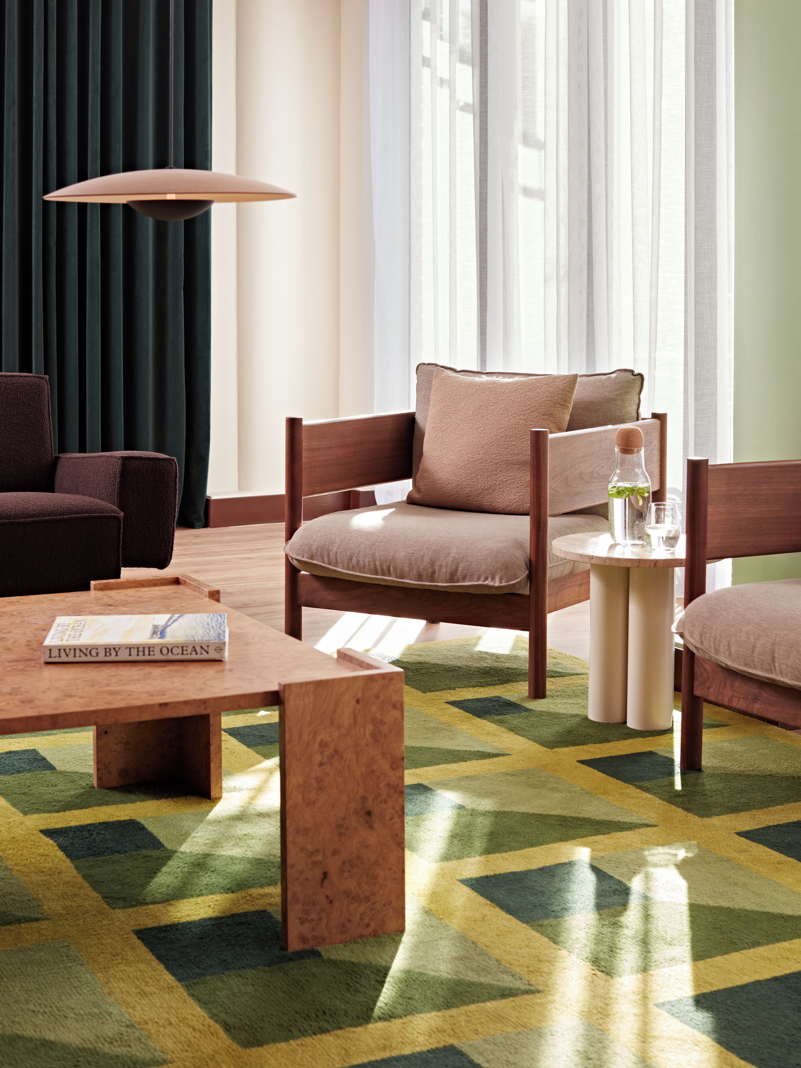 A modern hotel room with a sofa, armchairs, a coffee table, and a small side table.