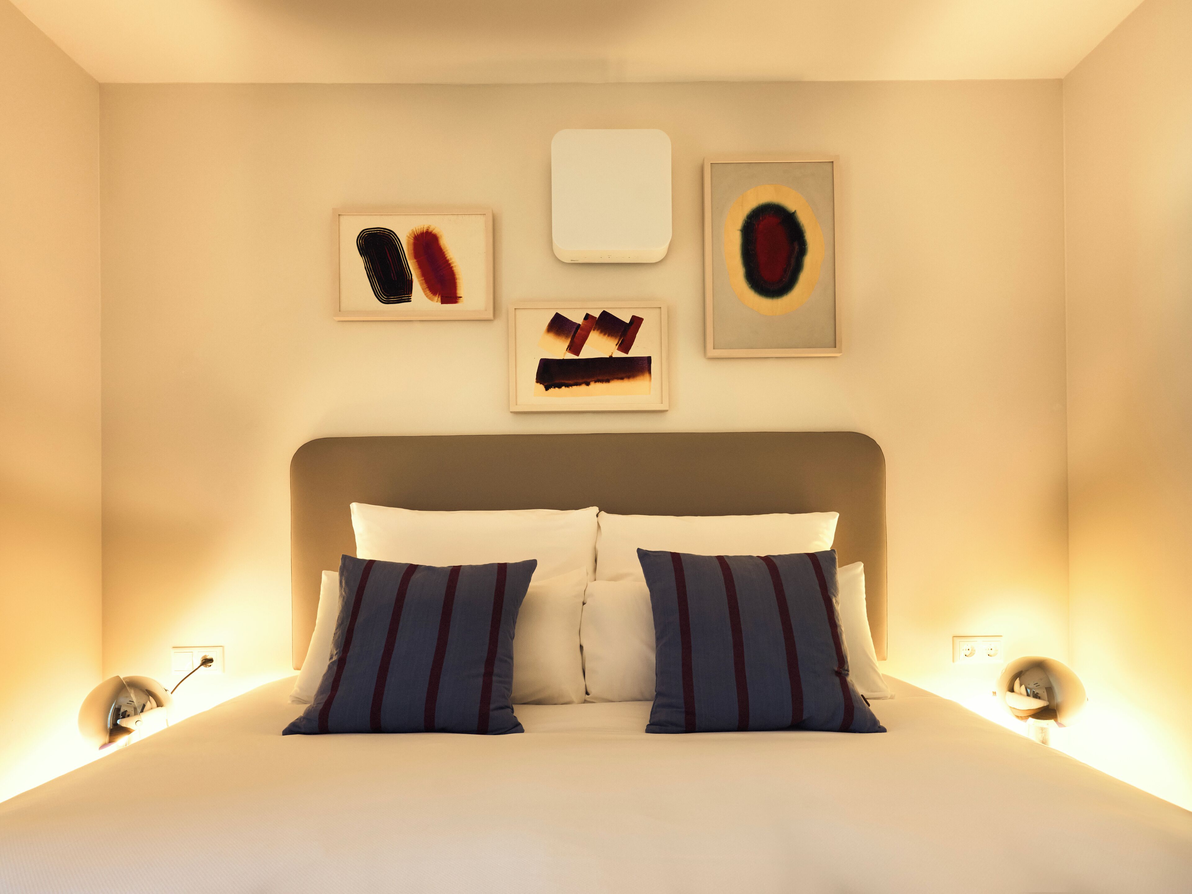 Un dormitorio ordenado con una cama grande, dos almohadas y tres obras de arte enmarcadas en la pared.