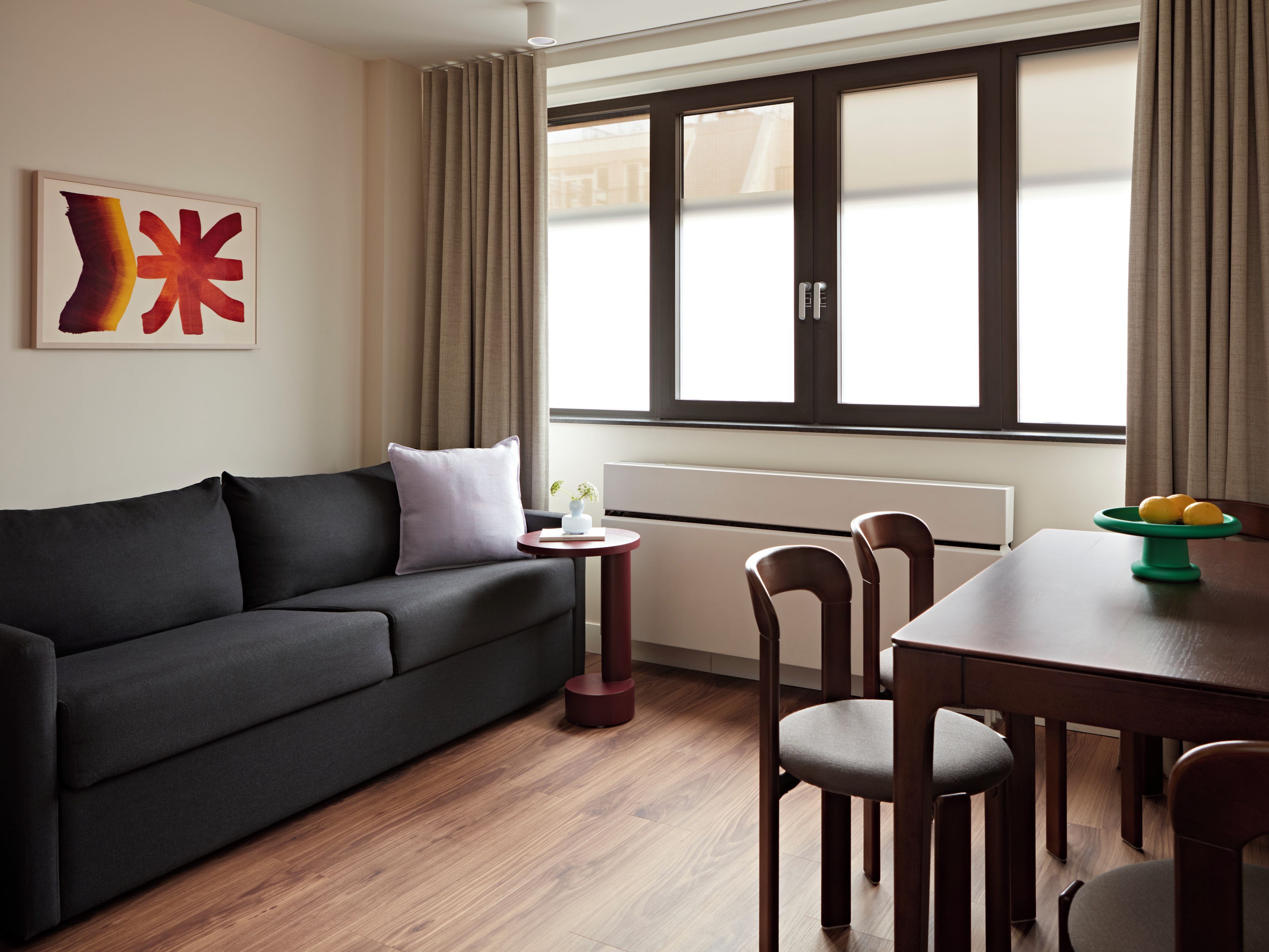 A modern living room with a dark sofa, a small round table, and a dining table with chairs.