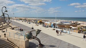 A seaside promenade with a sculpture, benches, and a beach in the background. - Numa The Hague Scheveningen (The Hague)
