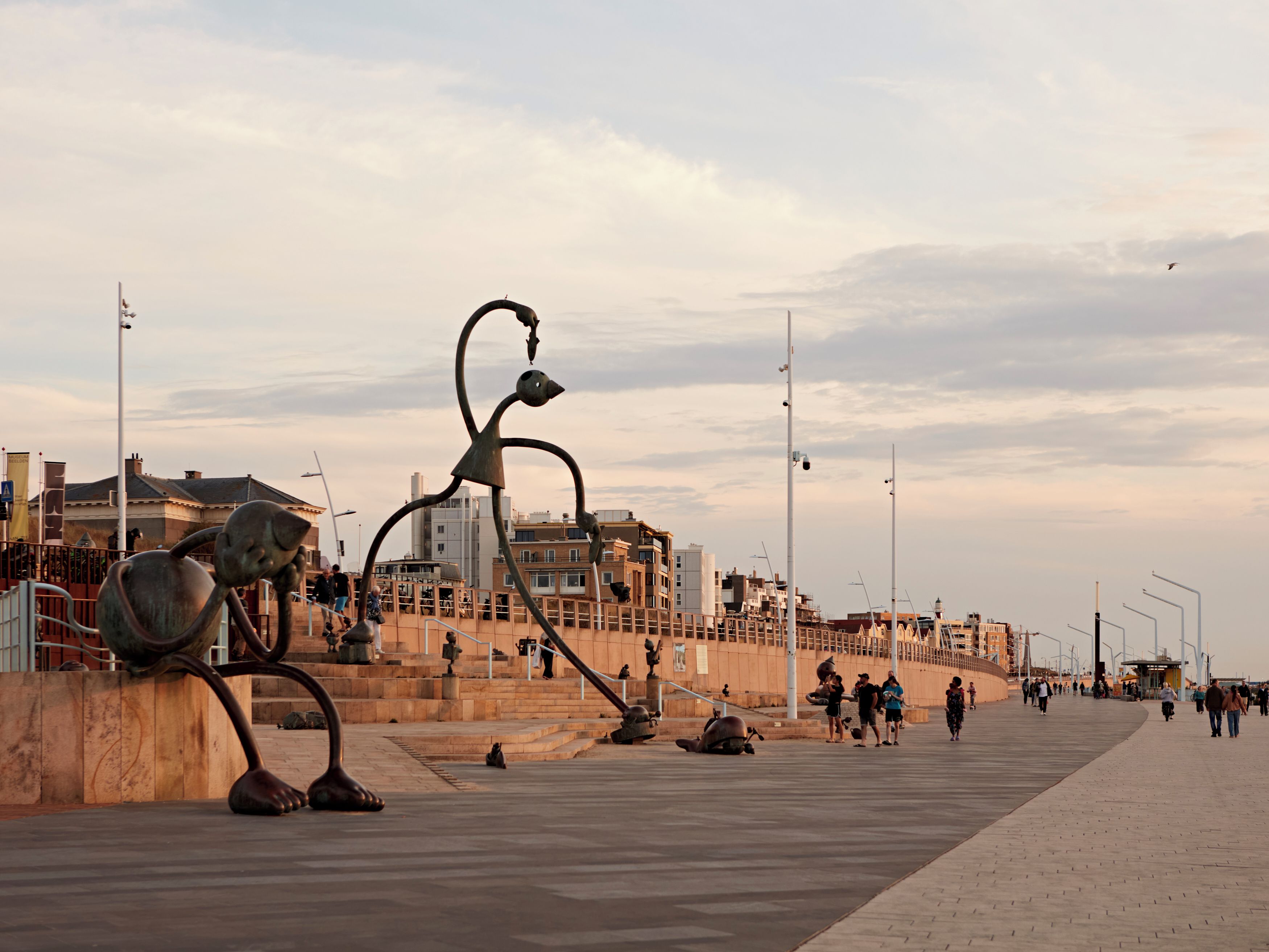 A public space with sculptures, a waterfront, and buildings in the background.