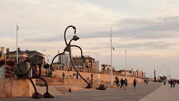 Un espacio público con esculturas, una ribera y edificios al fondo.