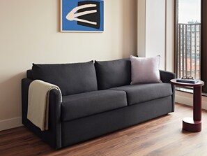 A modern living room with a dark grey sofa, a throw blanket, and a small round table with a book and glasses. - Numa The Hague Scheveningen (The Hague)