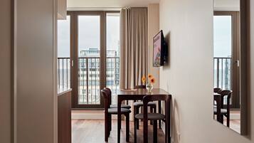 A modern hotel room with a balcony, a dining table with chairs, and a view of the cityscape.