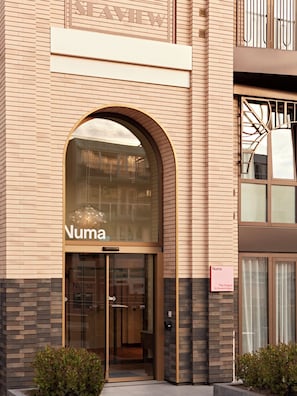 A building with a large arched entrance labeled 'Numa' and a sign indicating 'The Hague Scheveningen.' - Numa The Hague Scheveningen (The Hague)