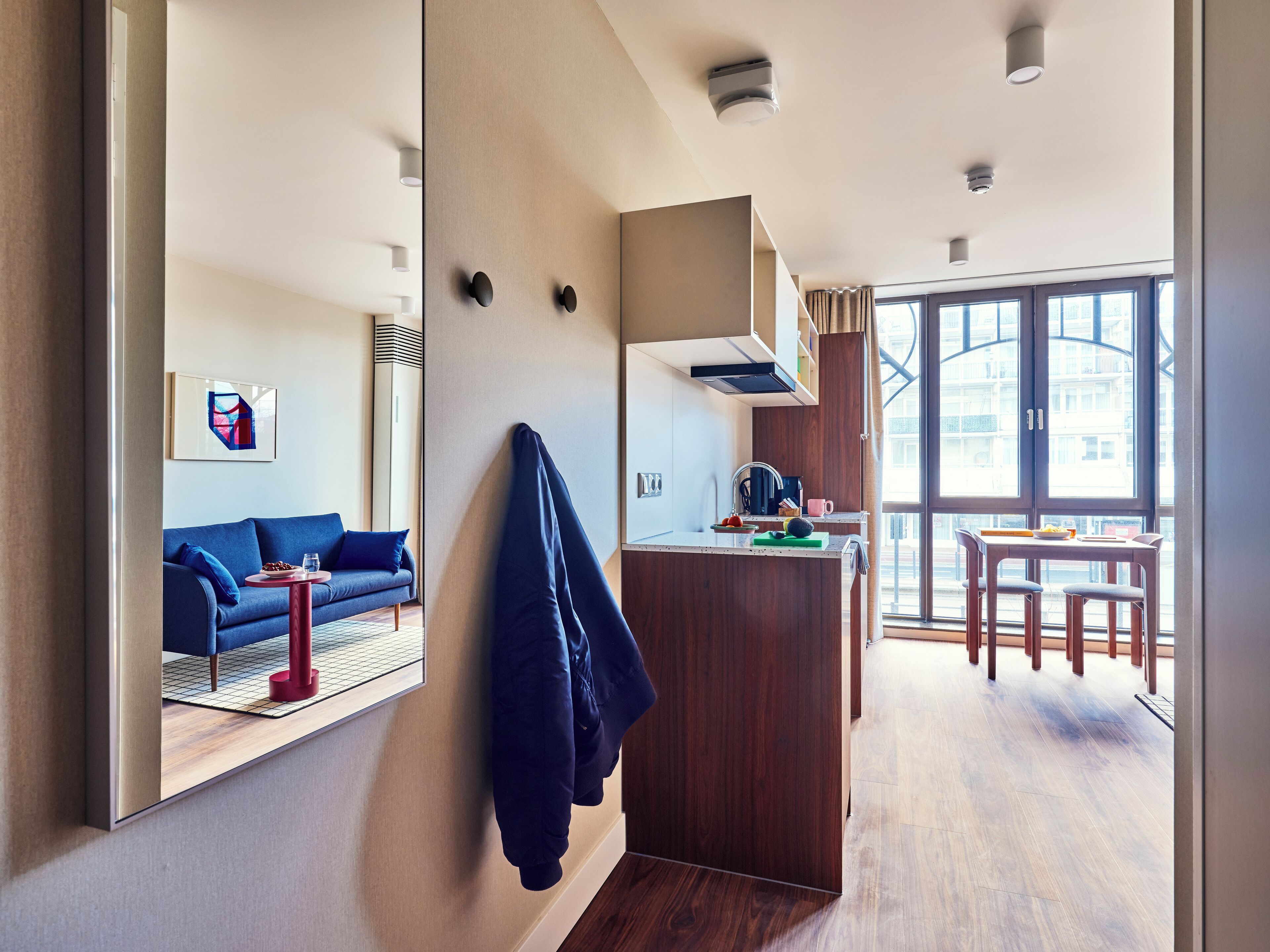 A modern hotel room with a living area, kitchenette, and large windows.