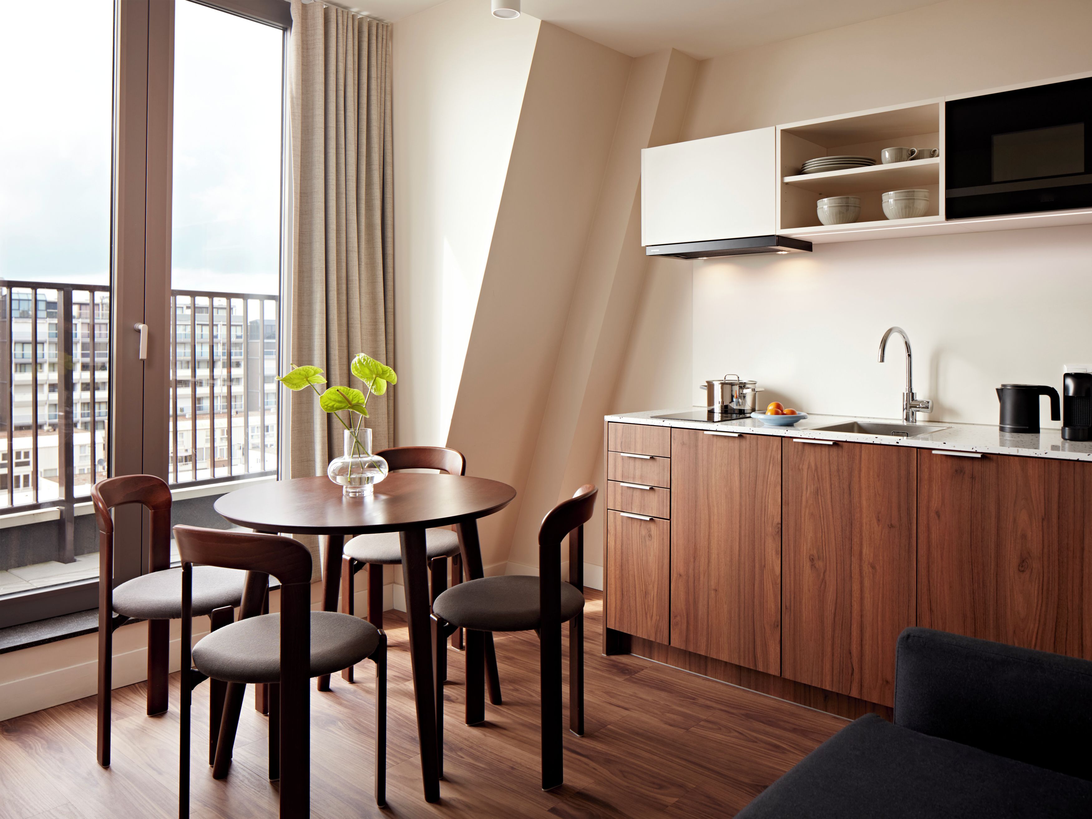 Une cuisine moderne avec un coin repas, des meubles en bois, un four encastré et une grande fenêtre avec des rideaux.