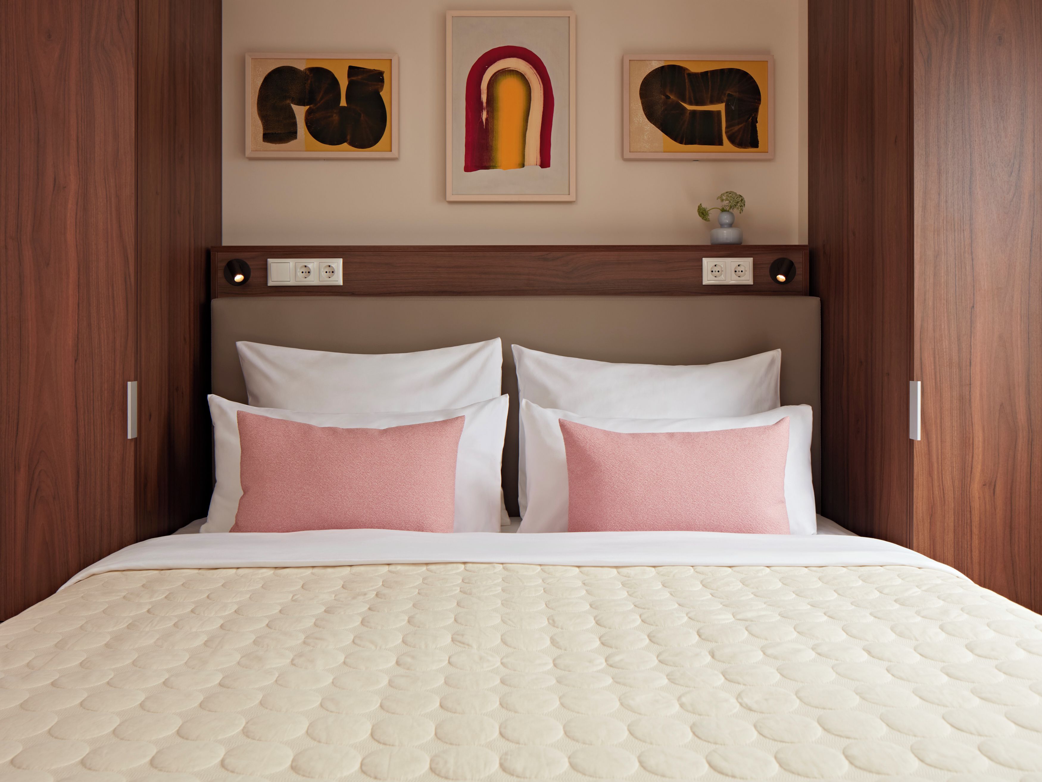 Un lit avec un matelas matelassé, deux oreillers et une tête de lit ornée d’œuvres d’art fixées au mur.