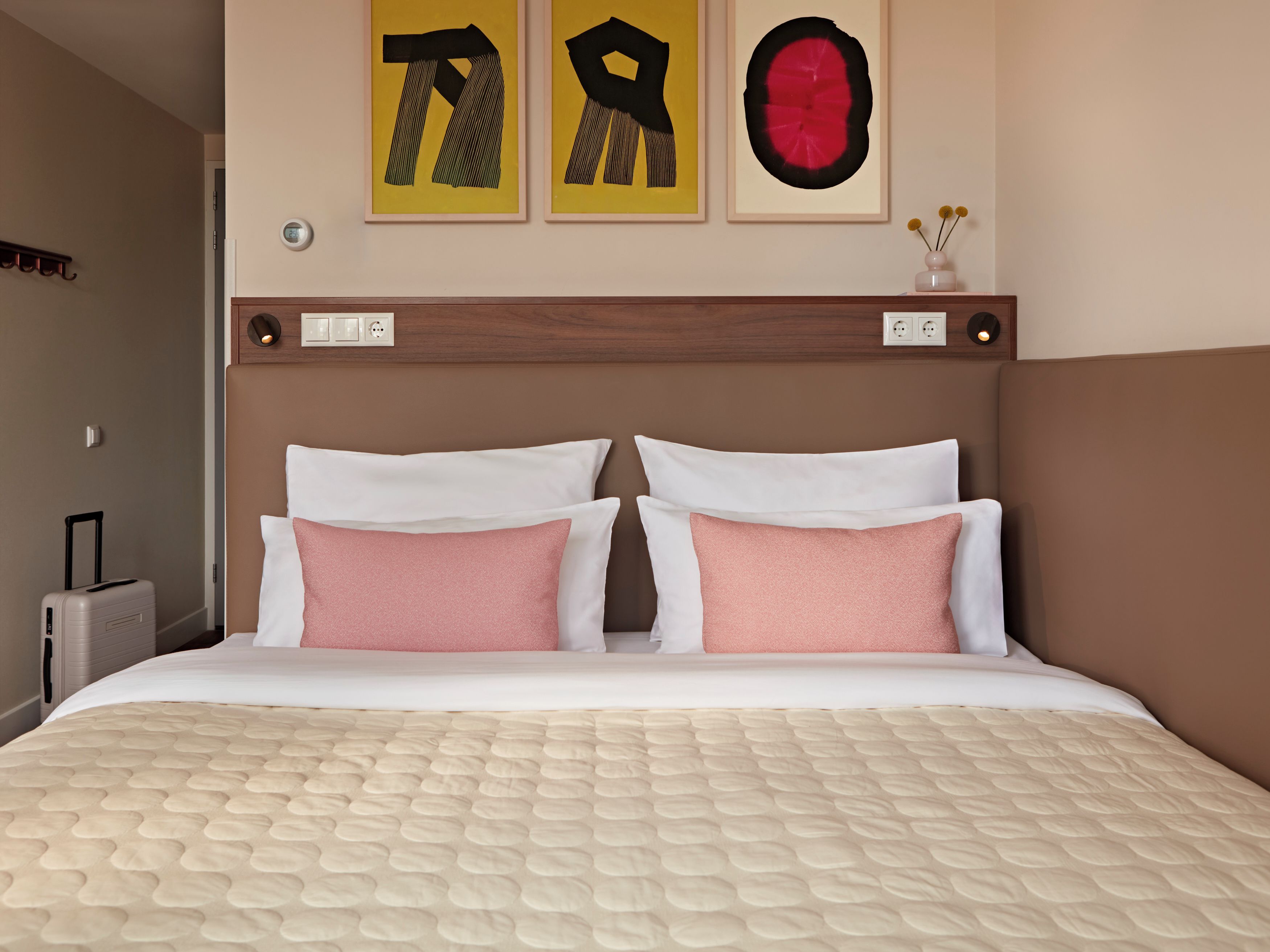 A hotel room with a bed, two pillows, a nightstand, a lamp, and artwork on the wall.