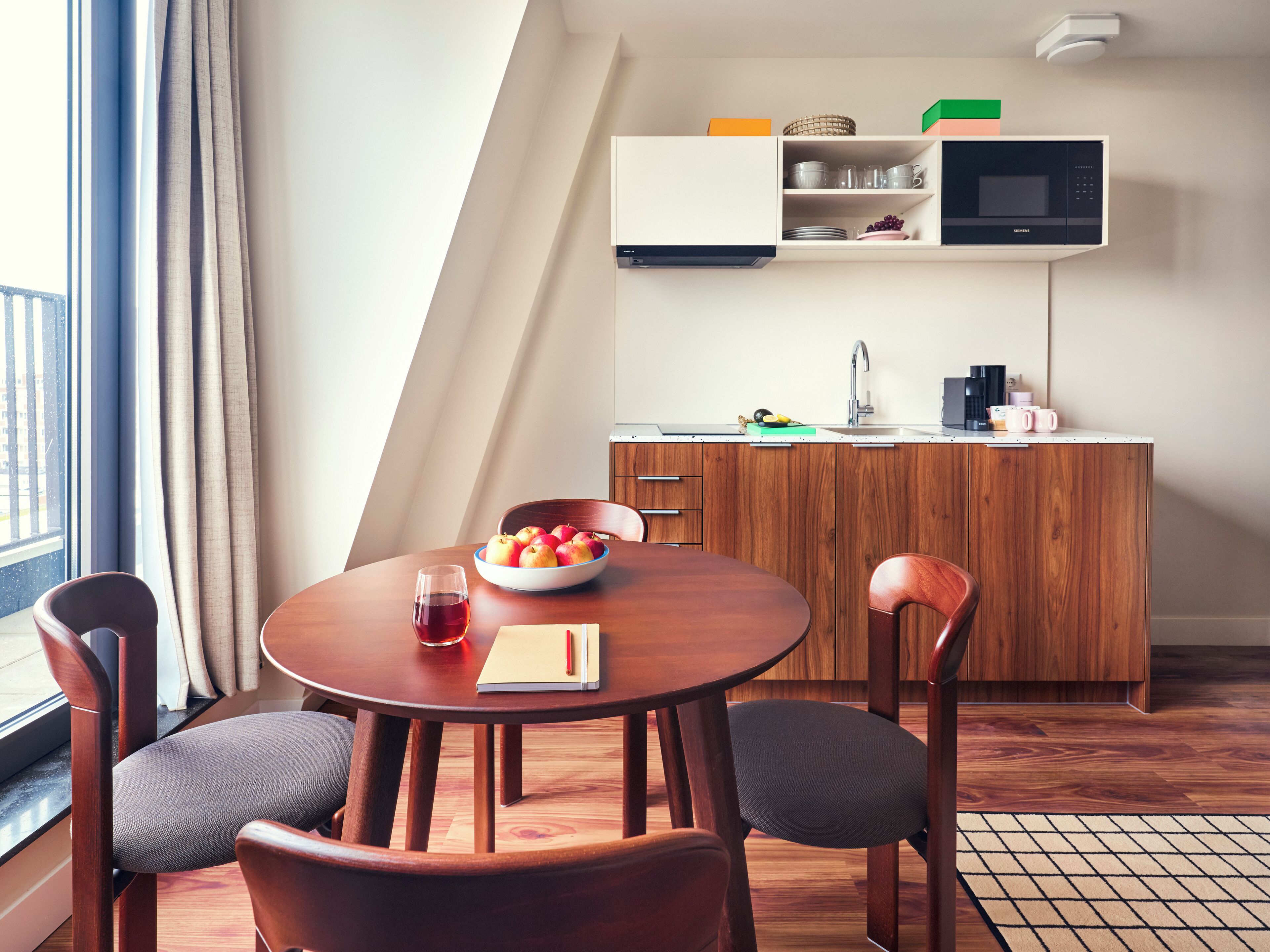 A modern kitchen with wooden cabinets, a dining table with chairs, and a bowl of fruit.