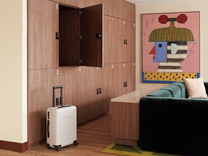 A hotel room with a wooden wardrobe, a single bed, a small table, a colorful abstract painting, and a suitcase. - Numa The Hague Scheveningen (The Hague)