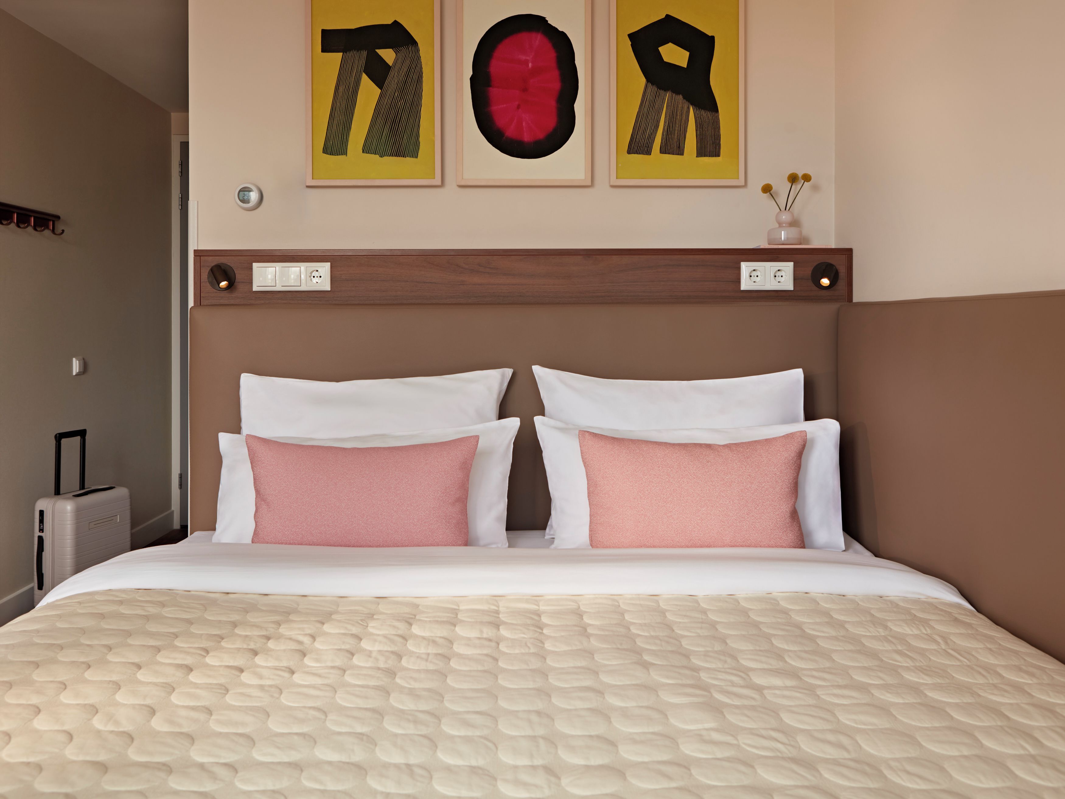 A hotel room with a bed, two pillows, a headboard, and three wall art pieces.