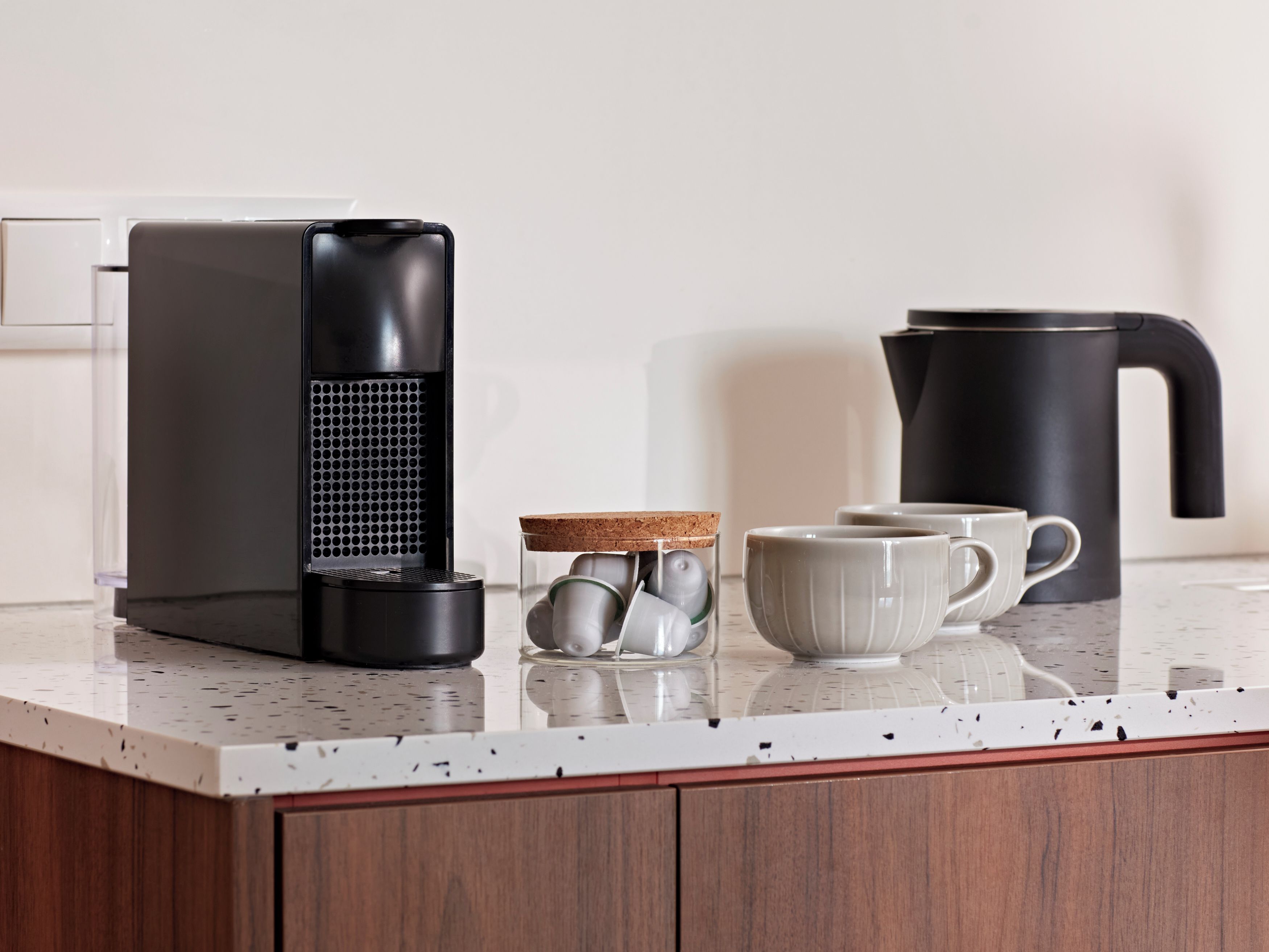 A kitchen counter with a coffee maker, a kettle, a mug, and a glass jar with tea bags.