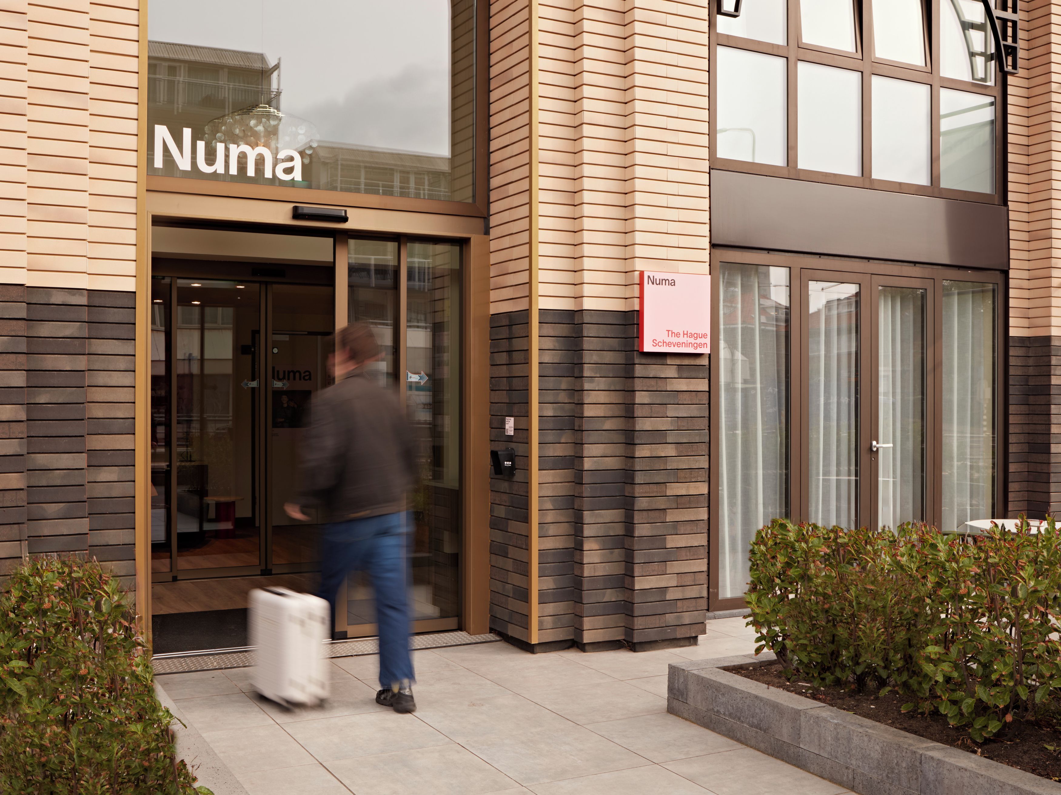 Een gevel met een bord waarop 'Numa' staat en een kleiner bord met 'Den Haag Scheveningen'.