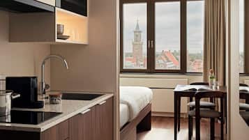 A compact hotel room with a kitchenette, a bed, a dining area, and a view of a clock tower through a window.